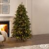 Un elegante albero di Natale artificiale di 180 cm con 1500 luci LED integrate, illuminato in una stanza accogliente. Il Pino Cristallo Illuminato 1500 Led di EDG Enzo de Gasperi presenta rami realistici e ignifughi, con un design facile da montare e diverse modalità di illuminazione. L'albero è posizionato accanto a un caminetto acceso, creando un'atmosfera festiva e calorosa.