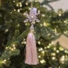Decorazione natalizia a forma di fiocco di neve con gemme rosa scintillanti, perla centrale e nappa setosa rosa cipria, appesa su un albero di Natale decorato.