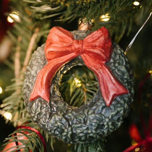 Ghirlanda natalizia verde con fiocco rosso, realizzata in plastica infrangibile, da appendere come decorazione festiva.
