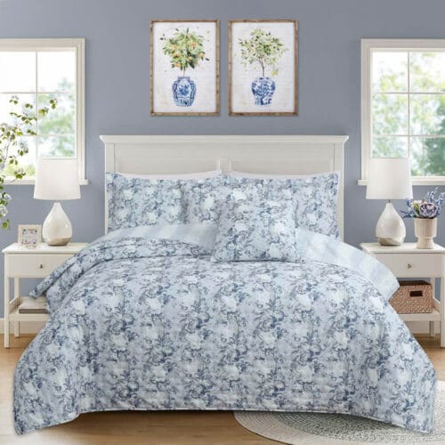 Set letto composto da una trapunta matrimoniale e due copriguanciali in tessuto floreale blu e bianco, ambientato in una camera shabby chic.