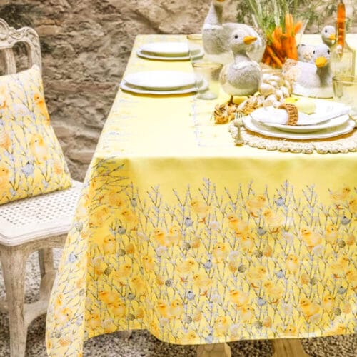 Tovaglia pasquale Blanc Mariclò 145x220 cm in poliestere, decorata con motivi di pulcini e fiori su fondo giallo, ideale per decorare la tavola.