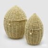 Set di due ceste in rattan intrecciato a forma di uovo, con coperchio e chiusura a cordino con bottone in legno, ideali per decorazioni pasquali o contenitori multiuso.