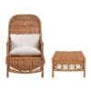 Poltrona in rattan con schienale alto e cuscini bianchi, accompagnata da uno sgabello coordinato con intreccio a vista.