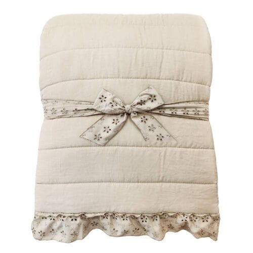 Trapunta beige matrimoniale con cuciture orizzontali e bordo decorato da una gala in pizzo Sangallo, confezionata con fiocco tono su tono.