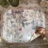 Tovaglietta in vinile ottagonale con sfondo crema, decoro natalizio vintage con fiocchi, palline e agrifogli. Finitura effetto legno.