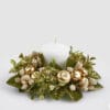 Corona decorativa con foglie verdi, bacche chiare glitterate e mele dorate intorno a una candela bianca.