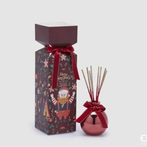 Profumatore rosso a sfera con fiocco in velluto e bastoncini glitterati, accanto a scatola decorata con Babbo Natale.