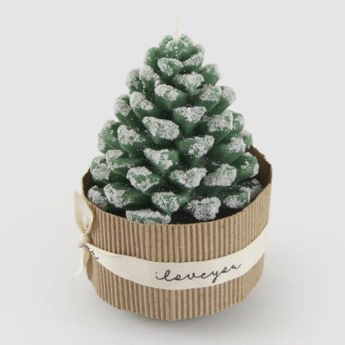 Candela verde a forma di pigna innevata, confezionata con supporto in cartone e nastro decorativo.
