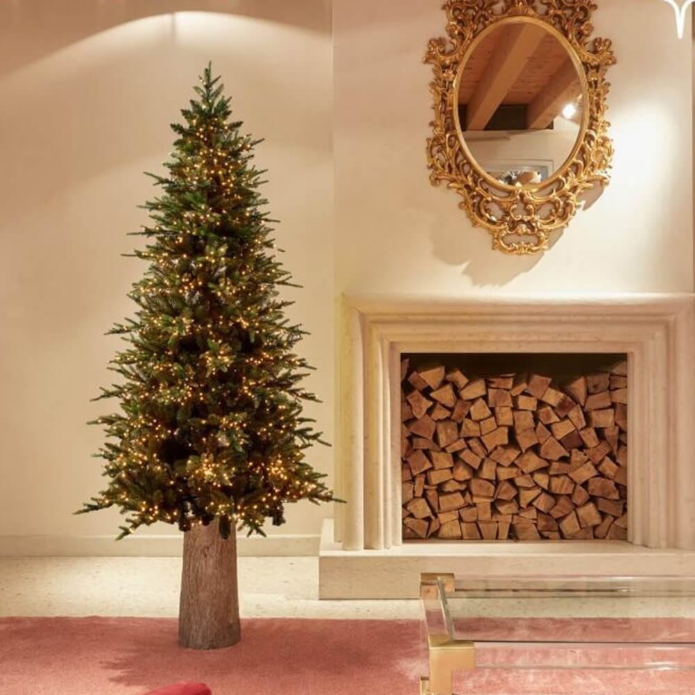 Albero di Natale artificiale EDG alto 180 cm con rami folti e 2000 luci LED calde, montato su base effetto tronco.