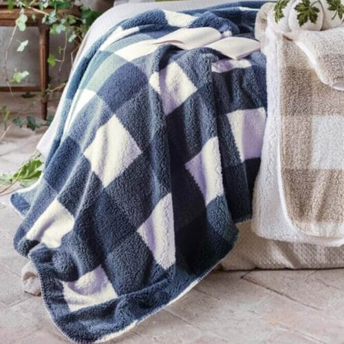 Plaid sherpa Blanc Mariclò con motivo a quadri nei toni azzurro e panna, effetto peluche, su letto elegante.