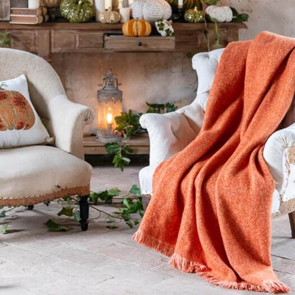 Plaid orange en tissu mélangé avec des franges, posé sur un fauteuil de style shabby dans un décor automnal agrémenté de citrouilles.