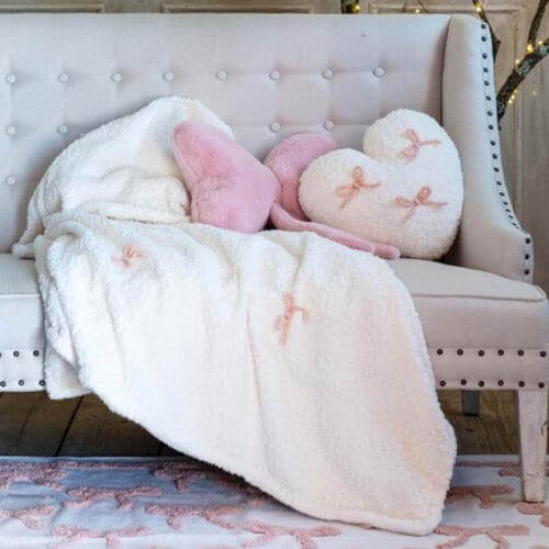Set composto da plaid pile bianco e cuscino cuore peluche con fiocchi rosa, stile romantico e coccoloso.
