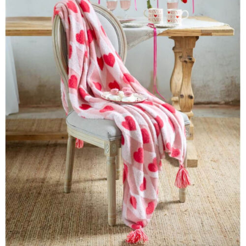 Plaid rosa con fantasia a cuori fucsia e rombi, rifinito con frange a nappine alle estremità, stile pop romantico.