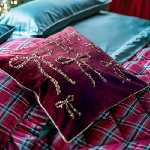 Cuscino in velluto bordeaux con ricami dorati a forma di fiocchi, decorato con paillettes, della collezione Nastro d’Oro.