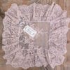 Centrino quadrato in pizzo cipria con ricami floreali e volant plissettato, stile shabby chic, su tavolo in legno rustico.
