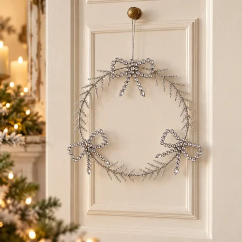 Ghirlanda circolare in metallo con rametti glitterati e tre fiocchi decorativi in cristalli trasparenti. Finitura luminosa e raffinata.