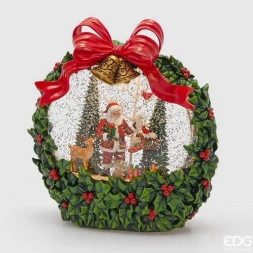 Carillón navideño en forma de corona con bola de cristal que contiene a Papá Noel, renos y árboles nevados, decorado con acebo y cinta roja.