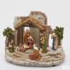 Crèche EDG avec cabane et ruines en résine, éclairée par LED, avec personnages en costumes colorés et scènes en mouvement, socle rond en pierre.