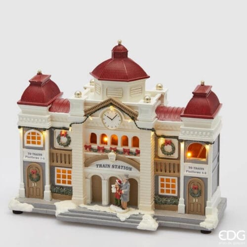 Stazione natalizia EDG in stile vittoriano con tetti rossi, orologio centrale, luci LED, ghirlande e figure davanti all’ingresso innevato.