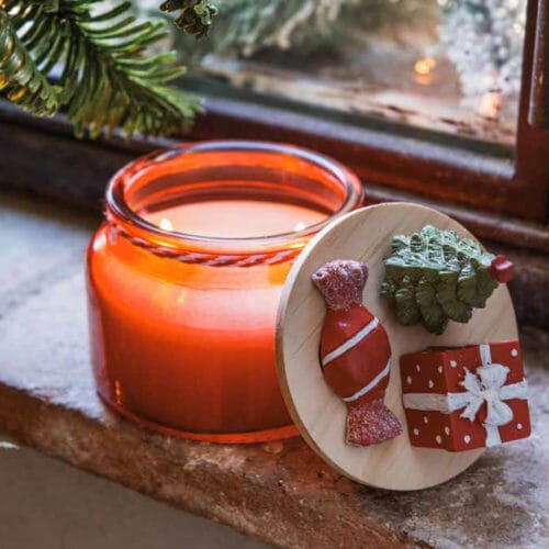 Candela natalizia rossa in vetro con coperchio in legno decorato con albero di Natale, regalo e caramella.