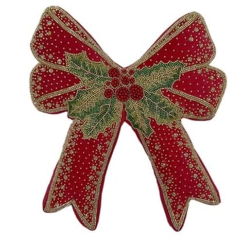 Cuscino rosso natalizio a forma di fiocco, decorato con agrifoglio e ricami oro, su poltrona bianca elegante.