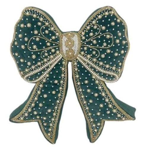 Cuscino natalizio verde a forma di fiocco, decorato con perline e dettagli oro, su poltrona imbottita bianca.