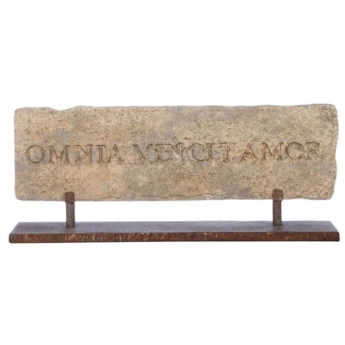 Stele decorativa in resina con scritta latina "Omnia Vincit Amor" e base in metallo brunito.