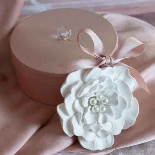 Decorazione profumata in gesso bianco a forma di fiore, con perle centrali e nastro rosa, presentata in elegante scatola tonda rosa cipria.