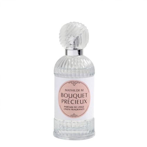 Flacone in vetro trasparente decorato con tappo zigrinato e etichetta rosa del profumo per tessuti Mathilde M Bouquet Précieux da 75 ml.