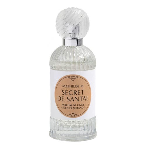 Flacone trasparente in vetro lavorato con tappo decorativo e etichetta color beige, contenente il profumo per tessuti Mathilde M Secret de Santal.