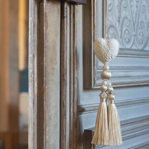 Nappa profumata color avorio con cuore in gesso decorato, perle e frange, confezionata in elegante scatola a righe color crema.