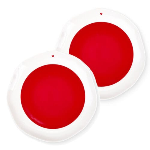 Coppia di piatti in porcellana bianca con centro rosso brillante e piccolo cuore rosso sul bordo, forma irregolare e moderna.