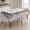 Tovaglia bianca con stampa e ricamo natalizio: rami di agrifoglio, palline decorative e fiocchi rossi lungo il bordo.