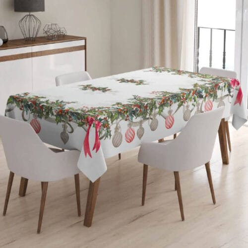 Tovaglia bianca con stampa e ricamo natalizio: rami di agrifoglio, palline decorative e fiocchi rossi lungo il bordo.