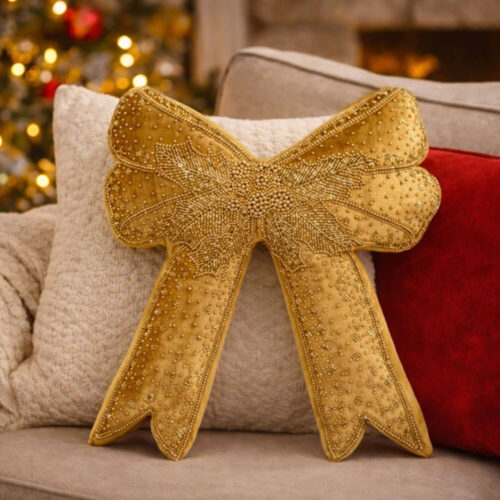 Cuscino decorativo dorato a forma di fiocco, impreziosito da ricami e perline, in un’atmosfera natalizia raffinata.