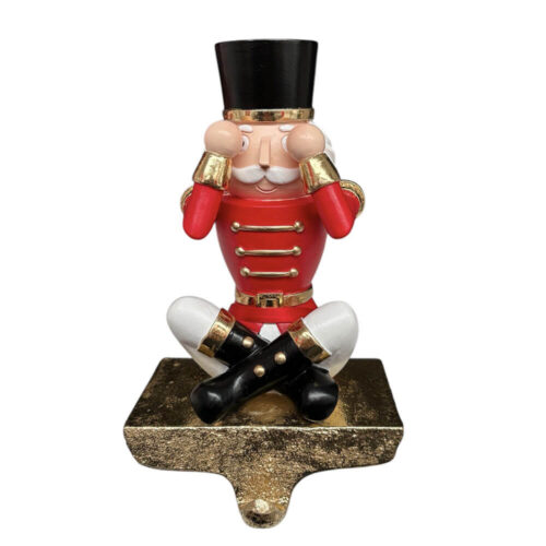 Gancio decorativo natalizio con schiaccianoci in posa “non vedo”, seduto con mani sugli occhi e base dorata per calze o presine.