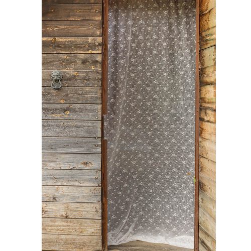 Tenda decorativa in tulle bianco con piccoli fiori e balza trasparente, montata su una porta in legno rustico.