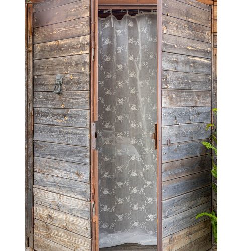 Rideaux décoratifs blancs en organza avec broderie de roses tissées et volant en voile, montés sur une porte en bois rustique.