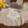Tovaglietta in cotone bianco con ricamo tono su tono e bordo smerlato, decorata con confetti bianchi in conchiglia argentata.