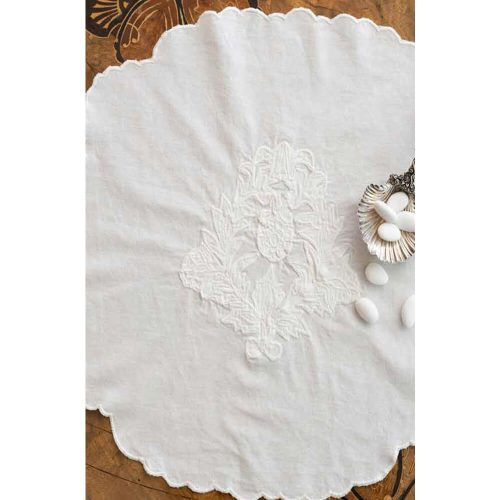 Tovaglietta in cotone bianco con ricamo tono su tono e bordo smerlato, decorata con confetti bianchi in conchiglia argentata.