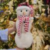 Pupazzo di neve decorativo in tessuto bouclé con cappello rosso a maglia e sciarpa a righe bianche e rosse.