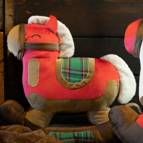 Cuscino rosso a forma di cavallo a dondolo con criniera bianca, sella in tessuto tartan e base imbottita marrone.