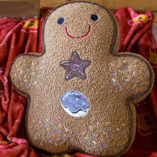 Cojín de jengibre marrón con adornos bordados de rocío de colores, estrella y caramelo.