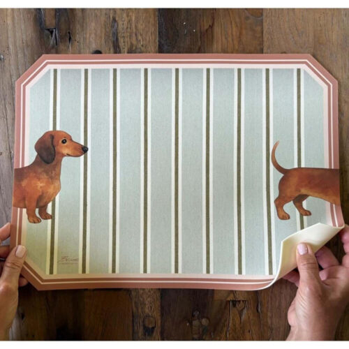 Mantel individual decorativo de vinilo con rayas verdes y contorno rosa, que representa un perro salchicha estilizado en los laterales.
