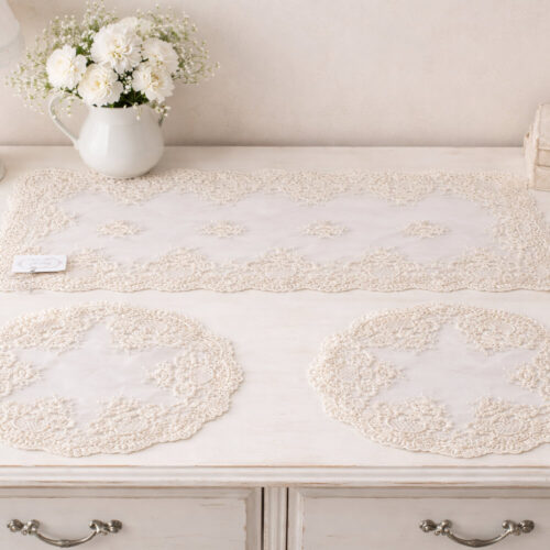 Tris di centrini Chez Moi Provenza color biscotto avorio con una striscia rettangolare e due centrini rotondi, realizzati in tulle trasparente con ricami floreali in rilievo e bordo smerlato decorativo.