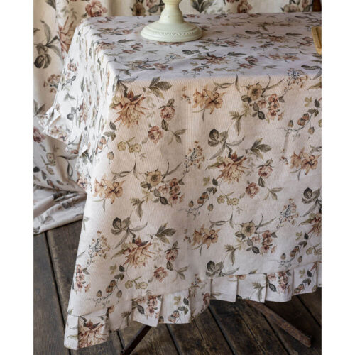 Tovaglia in cotone resinato color avorio con stampa floreale nei toni cipria e verde, bordata con balza arricciata coordinata.