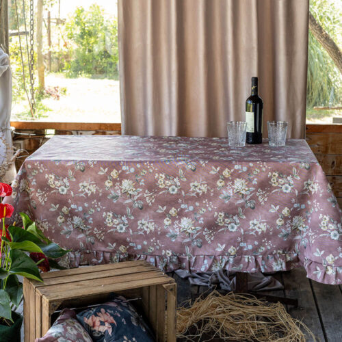 Tovaglia in cotone resinato color prugna con stampa floreale nei toni pastello e balza arricciata decorativa.