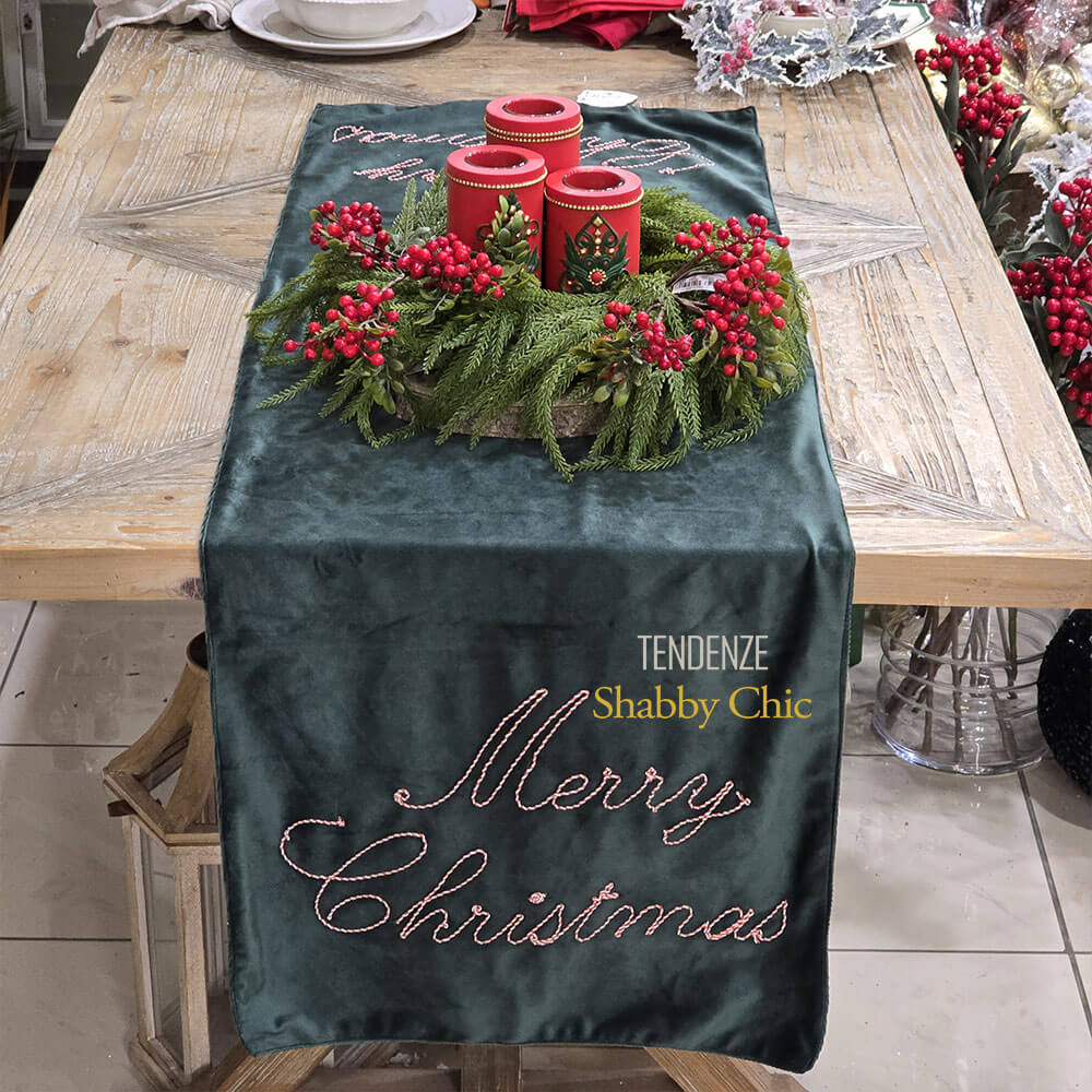 Chemin de table de Noël en velours vert avec "Joyeux Noël" écrit dans un galon rouge et blanc, sur une table en bois décorée d'un centre de table rouge et vert.