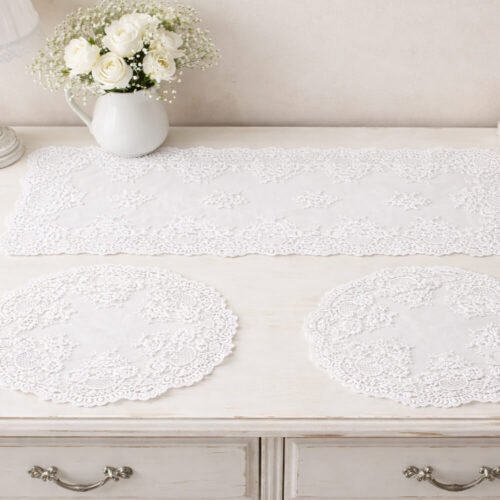 Tris di centrini bianchi in pizzo ricamato con motivi floreali e bordi smerlati, composto da una striscia rettangolare e due centrini rotondi.