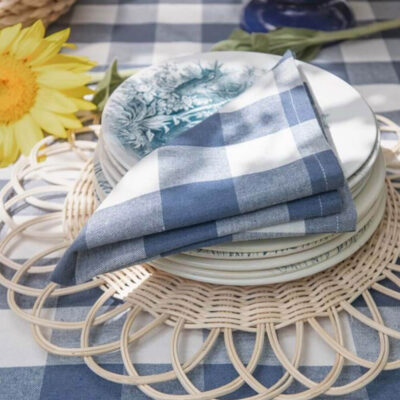 Serviette en tissu Vichy bleu et blanc, pliée et posée sur des assiettes décoratives dans un décor de table raffiné.